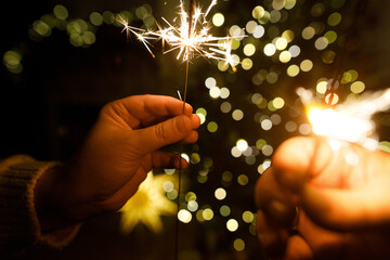 Happy New Year! Burning sparklers in hands on background of christmas tree golden lights bokeh at night. Glowing fireworks in couple hands, new year eve holiday celebration