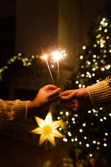 Happy New Year! Burning sparklers in hands on background of christmas tree golden lights bokeh at night. Glowing fireworks in couple hands, new year eve holiday celebration © sonyachny