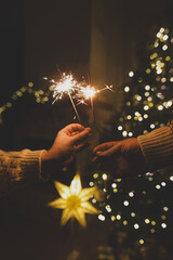 Happy New Year! Burning sparklers in hands on background of christmas tree golden lights bokeh at night. Glowing fireworks in couple hands, new year eve holiday celebration