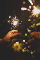 Happy New Year! Burning sparklers in hands on background of christmas tree golden lights bokeh at...