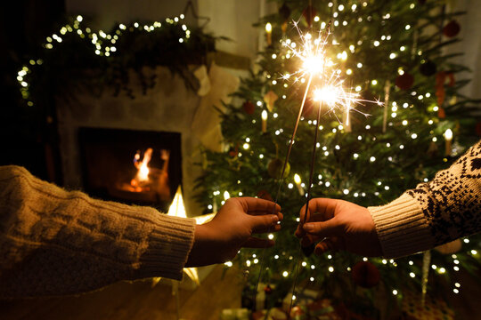 Happy New Year! Burning sparklers in hands on background of christmas tree golden lights at night. Glowing fireworks in couple hands, new year eve holiday celebration