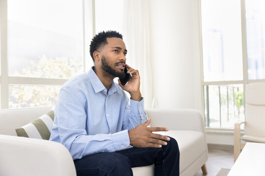 Confident young businessman speak on phone sitting on cozy couch