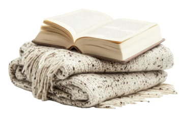 Book resting on a folded plaid blanket with fringes against white background