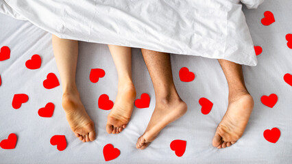Top view of millennial interracial couple resting after making love on bed, surrounded by red paper hearts. Overhead shot of passionate lovers relaxing after sex. Romantic intimacy concept