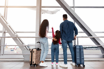 Cute Little Girl Standing With Parents In Airport Terminal, Looking At Plane Out Of Window, Rear...