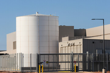Cylindrical storage tank positioned outside a large data center campus with perimeter fencing and...
