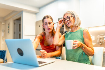 Women having fun watching streaming content on laptop in kitchen