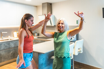 Joyful mother and daughter dancing in kitchen