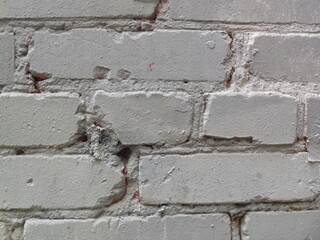 The old brick wall is painted white. The surface has defects, cracks, and stains.