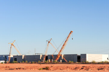 Cranes position steel and concrete panels during construction of a large industrial building, with...