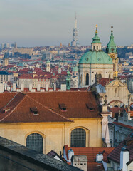 Fototapeta premium Panoramic view of historic european city with red rooftops and green domed church under soft evening light.