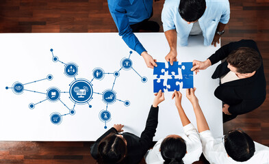 A diverse group of professionals engage in a collaborative meeting, assembling puzzle pieces while interacting with digital icons, symbolizing teamwork and innovative problem-solving. Amity