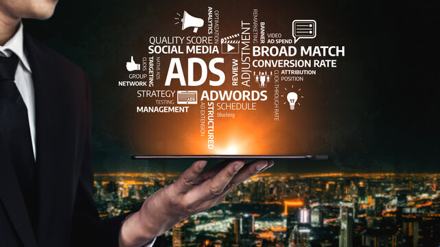 A businessman holds a tablet showcasing essential marketing terms against a vibrant cityscape background, highlighting modern advertising strategies and digital engagement. Tessel - Powered by Adobe