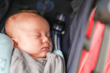A baby is sleeping in a stroller. The stroller is red and blue. The baby is wrapped in a blanket