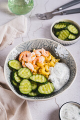 Pasta with shrimps, fresh cucumber and creamy sauce in a bowl on the table vertical view