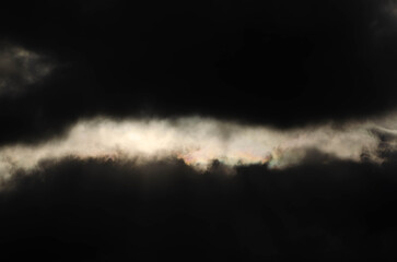 Dark storm clouds with bright illuminated gap and iridescent light