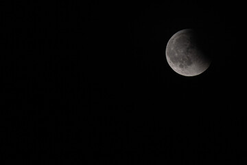 La lune partiellement visible dans un ciel nocturne très sombre, avec des nuages fins...