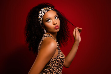 Flirty young woman posing confidently against a red backdrop wearing a leopard print outfit and...