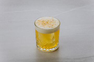 Creamy yellow cocktail in a textured glass with foam and nutmeg garnish on top