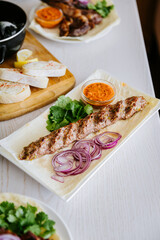 Traditional kebab with herbs, red onion and sauce on lavash, served on a white plate