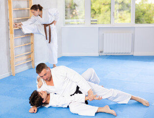 Judo or jiu-jitsu classes - two men practicing grabbing and throwing on sports mats under the...