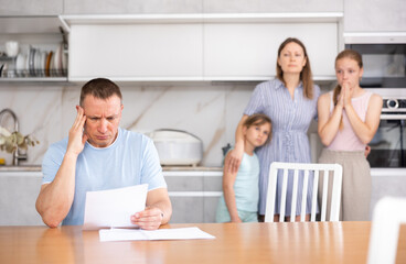 Disgruntled father carefully reads documents. The whole family stands in fear in the background