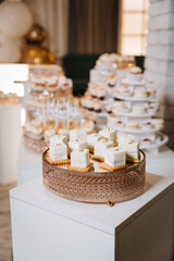 Elegant dessert table with white mousse cubes on cookies in luxury golden trays