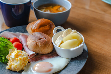 Western style breakfast with bread, fried egg, ham, salad, banana, and coffee
