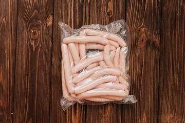 Vacuum packed chicken sausages on wooden table with tomatoes and salt in background