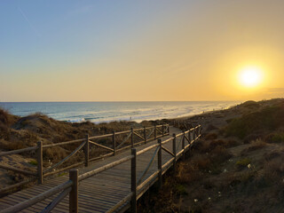 sunset at a coast with dunes near Marbella, wooden walkway to the Mediterranean Sea, Costa del Sol in the summer, Andalusia, Spain