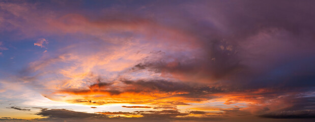 Colorful sunset sky with setting sun behind vivid orange and yellow clouds