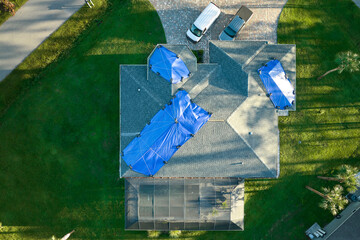 Top view of leaking house roof covered with protective tarp sheets against rain water leaks until replacement of asphalt shingles. Damage of building rooftop as aftermath of hurricane Ian in Florida © bilanol