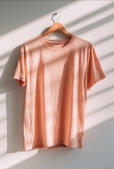 Cute peachcolored tshirt hanging on a white wall product photography natural lighting simple and clean background aesthetic colors professional photoshoot sty
