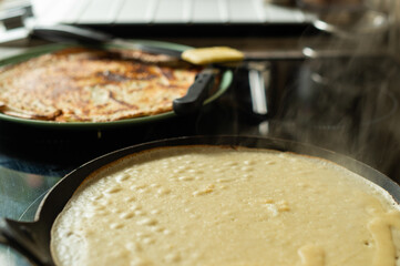 A pancake fries on a skillet, with a plate of ready pancakes and batter behind, perfect for cooking vibes. Ideal for food visuals, home recipes, or cozy lifestyle content with a warm appeal. 