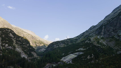 Swiss Alps with houses, winding road, clouds, and overcast sky, captured by drone. Schweizer Alpen mit Häusern, kurviger Straße, Wolken und bedecktem Himmel, aufgenommen mit Drohne.