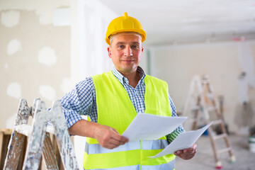 Man with documents in her hands stands in the middle of renovated room in a cottage