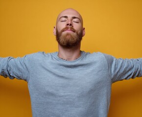 Relaxed man with a beard, arms outstretched, against a vibrant yellow backdrop, exudes tranquility and calm.