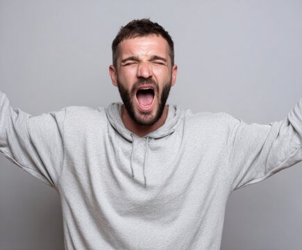 A man in a light gray hoodie expresses intense emotion with his mouth wide open in a dramatic, expressive portrait.