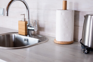 Minimalistic Scandinavian kitchen interior featuring a sleek sink, wooden paper towel holder, and modern kettle, creating a bright and functional atmosphere with copy space
