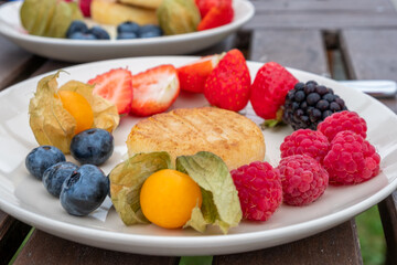 Fresh and vibrant plate of assorted berries, golden berries, and a round cake, showcasing a colorful and healthy dessert arrangement with energizing appeal