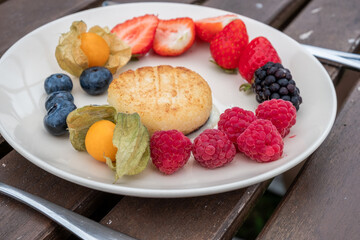 Fresh cheese, pancakes platter featuring vibrant strawberries, blueberries, raspberries, and a golden cake, arranged beautifully on a white plate, showcasing healthy and energizing food options