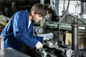 Guy worker at metallurgical plant drills hole in metal plate using a drilling machine