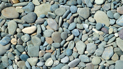 Pebbles stones on seashore as  texture background for design of web banner template page. many stones and they are different in color and size, dry stones illuminated by sun