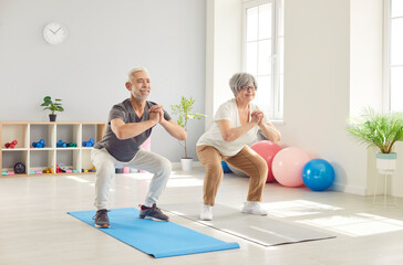 Active happy old senior doing squat morning exercise, sporty people practicing yoga lesson in gym,...