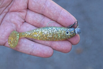 hand holds one yellow silicone fish with steel fishing hook in the summer street