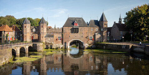 Wide angle panorama of the double gated medieval city entrance Koppelpoort structure reflecting in the Rijn canal water in the foreground on a sunny day