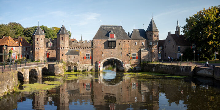 Wide angle panorama of the double gated medieval city entrance Koppelpoort structure reflecting in the Rijn canal water in the foreground on a sunny day