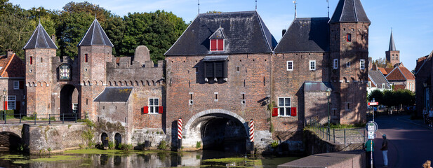 Wide angle panorama of the double gated medieval city entrance Koppelpoort structure reflecting in the Rijn canal water in the foreground on a sunny day