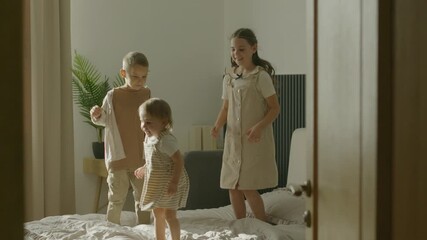 Three happy kids are jumping on a bed in a sunny room. Joyful children playing together in the bedroom, enjoying their day. - Powered by Adobe