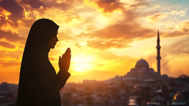 Silhouette of a woman praying at sunset, near a mosque.